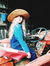 Girl wearing straw hat while sitting on tractor in barn