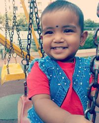 Close-up portrait of happy boy on swing at playground