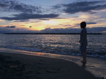 Silhouette man standing on beach against sky during sunset