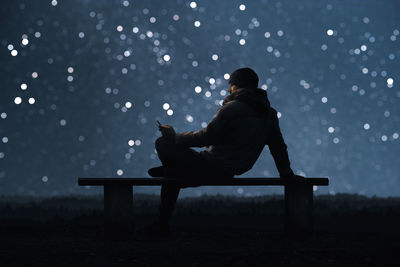 Man using phone while sitting on seat against star field