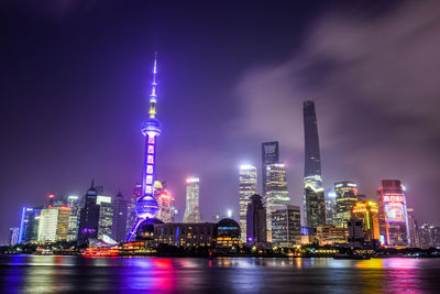 Illuminated oriental pearl tower in city by river huangpu at night