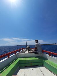 Man sitting on railing by sea against sky