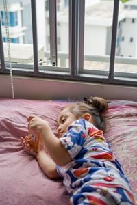 Cute little girl is watching videos on smartphone on the bed.