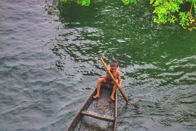 High angle view of shirtless boy sitting in boat on river