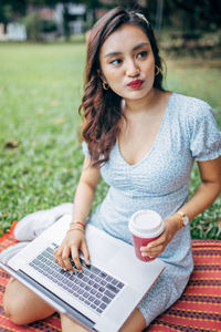Beautiful woman using laptop holding coffee cup sitting at park