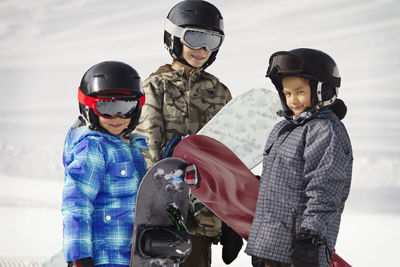 Siblings carrying snowboards while standing on snow covered field