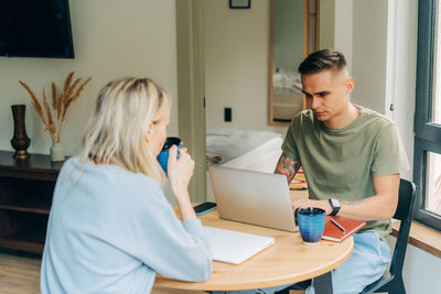 A young married couple uses a laptop at breakfast and drinks coffee.