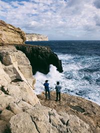 Rear view of friends standing on cliff by sea against sky