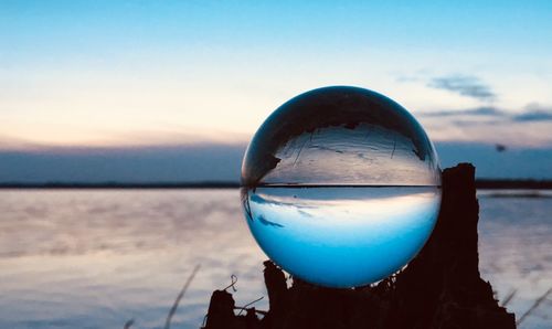 Close-up of crystal ball on beach against sky during sunset