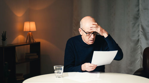 Elderly man sitting at the table reads his electricity and gas bills
