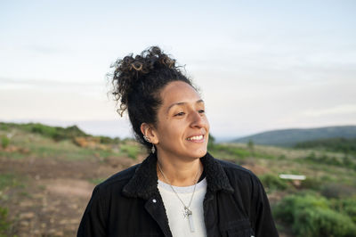 Woman smiling while standing outdoors in nature.