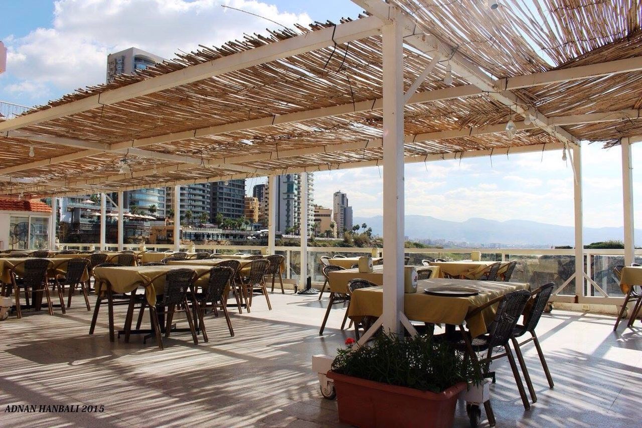 built structure, architecture, building exterior, chair, sky, table, absence, sunlight, roof, restaurant, empty, day, parasol, tourist resort, incidental people, travel destinations, outdoors, cloud - sky, shadow, sunshade