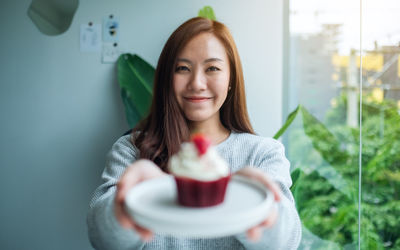 A beautiful asian woman holding a plate of red velvet cupcake