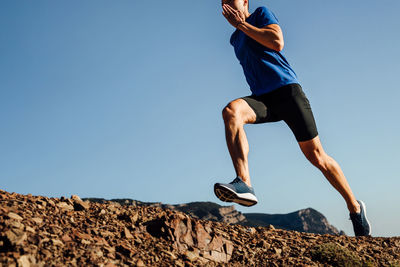 Low angle view of man jumping on rock against clear sky