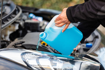 Cropped hands of mechanic pouring blue liquid in car engine