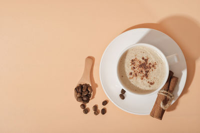 Cinnamon coffee cappuccino in white classic cup on beige background. top view