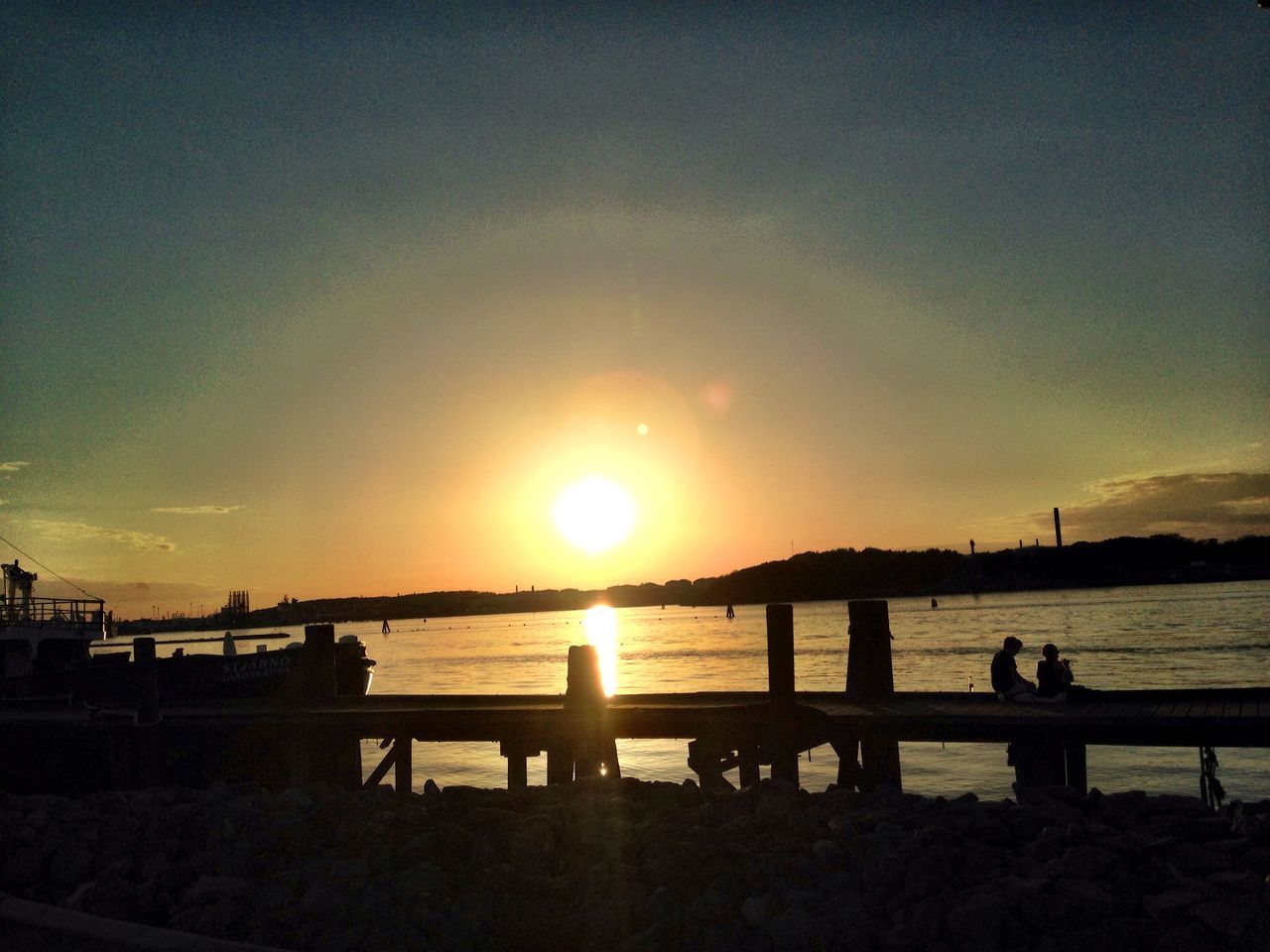 sunset, water, silhouette, sun, sea, scenics, tranquil scene, tranquility, beauty in nature, orange color, sky, nature, idyllic, pier, sunlight, reflection, horizon over water, incidental people, beach, railing