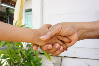 Cropped image of grandmother shaking hands with granddaughter against wall