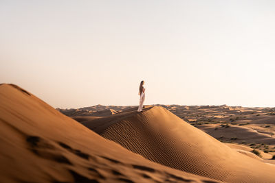 Rear view of man walking on sand at desert against clear sky