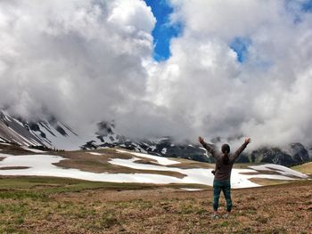 Rear view of hiker standing with arms raised against clouds covering mountains