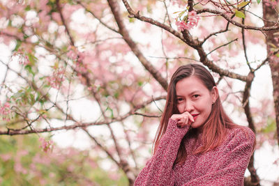 Mid adult woman wearing sweater while standing against cherry tree