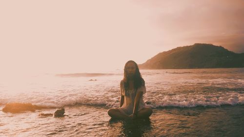 Woman sitting on shore at beach against sky