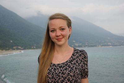 Portrait of smiling young woman standing in sea against mountains