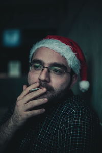 Thoughtful young man smoking cigarette while wearing santa hat at home