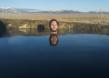 Man with eyes closed in calm lake against sky