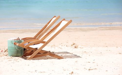 Folding chairs on beach against sky