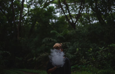 Man with smoke covering face standing against trees