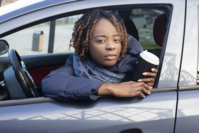 Portrait of mid young woman holding coffee cup while sitting in car