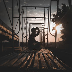 Side view of silhouette woman sitting on road against sky