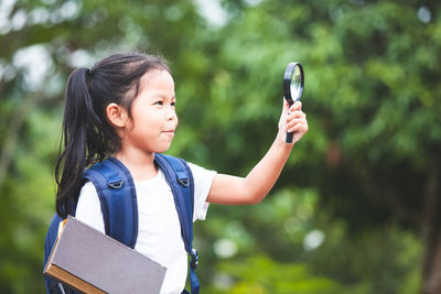 Smiling girl holding book and magnifying glass