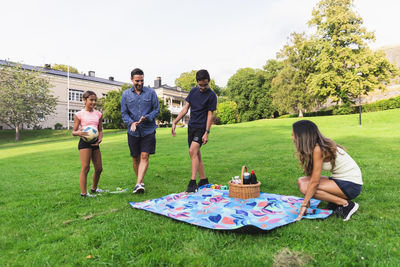 Woman laying out picnic blanket with family on grass in lawn