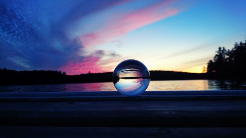 Close-up of crystal ball on water against sky during sunset