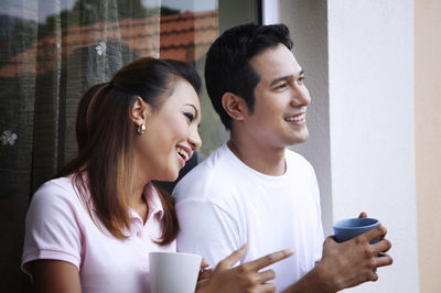 Smiling couple talking while having coffee against wall