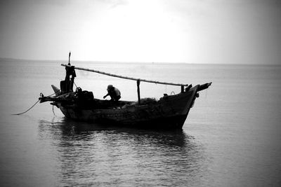 Man crouching in fishing boat on sea against sky