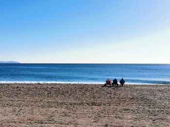 People sitting on beach against clear sky