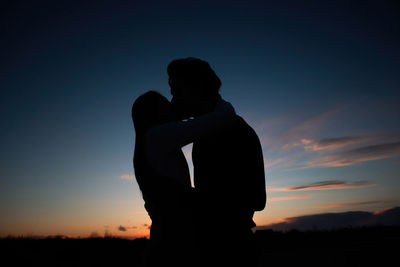 Young lovely couple hugging each other and kissing at orange sunset. silhouette at sunset background