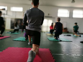 Rear view of people practicing on yoga mat in gym