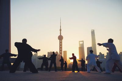 Men performing tai chi against oriental pearl tower during sunrise in city