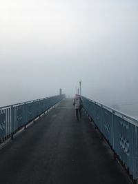 Rear view of woman walking on bridge, foggy morning 