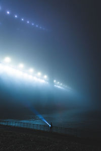 Man walking with flash light walking by railing against sky at night