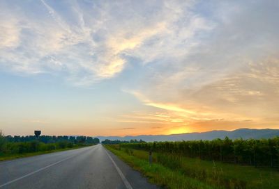 Road amidst field against sky during sunset