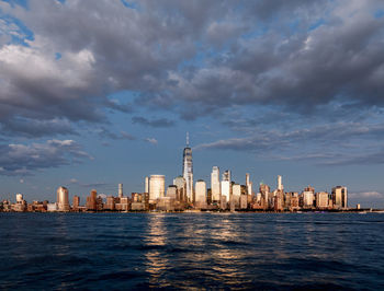 City at waterfront against cloudy sky