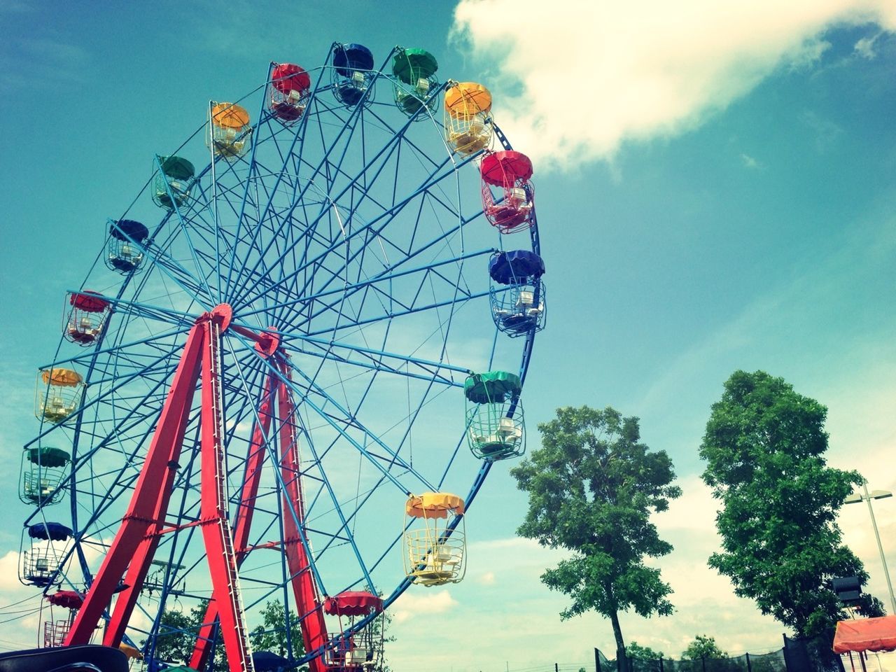 amusement park, amusement park ride, ferris wheel, arts culture and entertainment, low angle view, sky, tree, fun, enjoyment, multi colored, leisure activity, day, chain swing ride, flag, cloud - sky, large, built structure, outdoors, fairground ride, traveling carnival