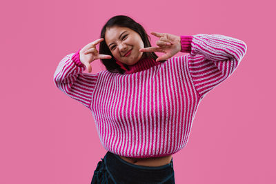 Portrait of young woman standing against pink background