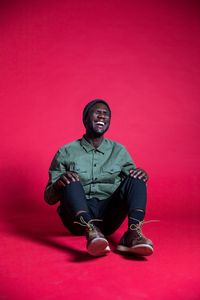 Portrait of young man sitting against pink background