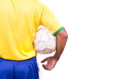 Midsection of man holding soccer ball while standing against white background